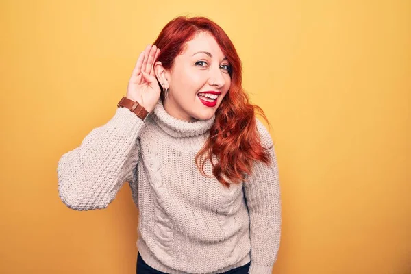 耳を傾け 噂やゴシップに耳を傾け手で笑みを浮かべて黄色の背景にカジュアルなタートルネックセーターを身に着けている若い美しい赤毛の女性 病気の概念 — ストック写真