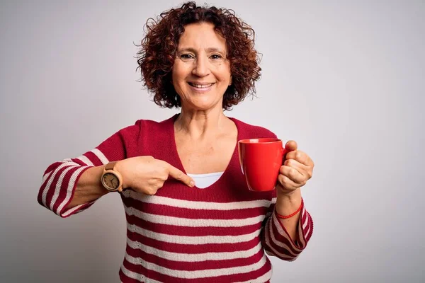 Middle age curly hair woman drinking mug of coffee over isolated white background with surprise face pointing finger to himself