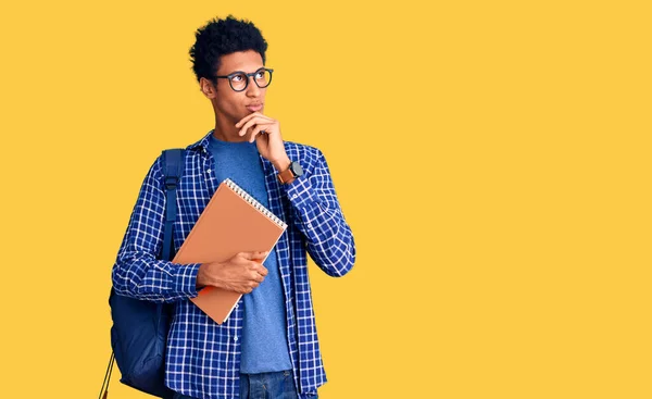 Joven Afroamericano Con Mochila Estudiante Sosteniendo Libro Con Mano Barbilla —  Fotos de Stock