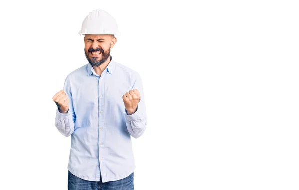 年轻英俊的男人戴着建筑师的硬礼帽 非常高兴 兴奋地举起双臂 做获奖者的手势 微笑着 尖叫着要成功 庆祝概念 — 图库照片