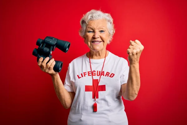 年长美丽的灰白头发的救生员女人用双筒和红色背景的哨子高喊着自豪 庆祝胜利和成功 非常兴奋 欢呼着感情 — 图库照片