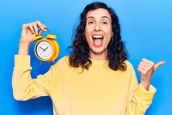 Çalar saati tutan genç, güzel İspanyol bir kadın baş parmağını yana kaldırmış, ağzı açık gülümsüyor. 