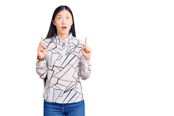 若いです美しい中国人女性身に着けているカジュアルシャツ驚きと驚きを見上げと指差すと指と上げ腕 — ストック写真