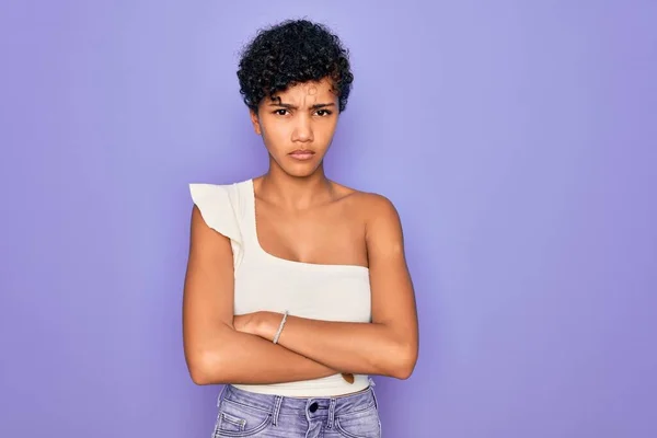紫の背景の上にカジュアルなTシャツを着た若い美しいアフリカ系アメリカ人アフロ女性は懐疑的で緊張し 両腕を組んで顔の表情を否定しています 負の人 — ストック写真
