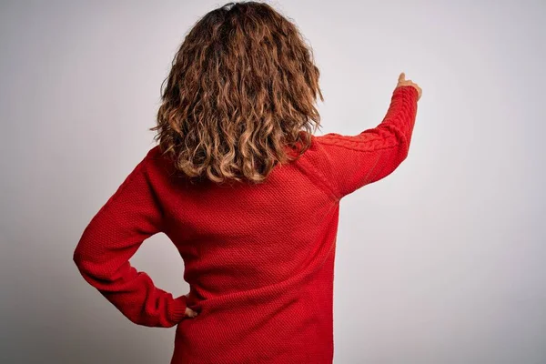 Orta yaşlı esmer kadın izole edilmiş beyaz arka planda dikilip parmak eliyle öne doğru poz veriyor.