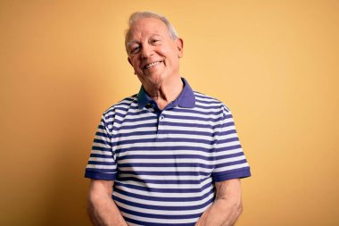 Gri saçlı, donanma çizgili tişört giyen, sarı arka planda duran, yüzünde ciddi bir ifadeyle rahatlamış yaşlı bir adam. Basit ve doğal bir şekilde kameraya bakıyorsun..