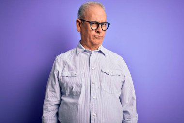 Orta yaşlı, beyaz, çizgili gömlek ve gözlük takan yakışıklı bir adam mor arka plan şüphecisi ve gergin, sorun yüzünden suratını asıyor. Negatif kişi.