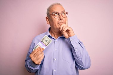 Orta yaşlı, ağarmış bir adam pembe arka planda bir deste banknot tutuyor. Ciddi bir yüz. Soru soruyor, kafası çok karışık.