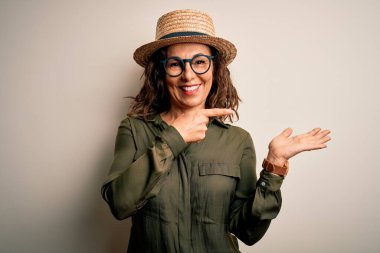 Orta yaşlı esmer kadın, gözlüklü ve şapkalı. İzole edilmiş beyaz arka planda duruyordu. Kameraya hayret ediyor ve gülümsüyordu..