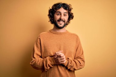 Sarı arka plan üzerinde rahat ve neşeli gülümseyerek el ele tutuşan sakallı genç yakışıklı bir adam. Başarı ve iyimser