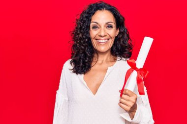 Orta yaşlı, diploma almış güzel bir kadın. Pozitif ve mutlu görünüyor. Kendine güvenen bir gülümsemeyle ayakta duruyor ve dişlerini gösteriyor. 