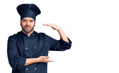 Genç İspanyol tencere üniforması giyen, elleri büyük ve büyük boy işareti gösteren, ölçü sembolü olan bir adam. Kameraya bakıp gülümsüyor. ölçüm kavramı. 