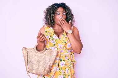 Genç Afro-Amerikan artı cüsseli kadın elinde sepet çantasıyla ağzıyla ağzını kapatıyor, şok geçiriyor ve hata yapmaktan korkuyor. şaşırmış ifade 