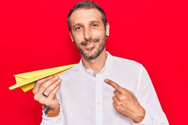 Elinde kağıt uçak tutan genç yakışıklı adam gülümsüyor. 