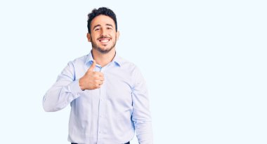 İş kıyafetleri giyen İspanyol genç adam elleriyle mutlu bir jest yapıyor. Kameraya bakıp başarıyı gösteren ifade. 