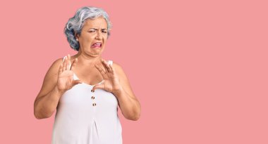 Son sınıf öğrencisi, gri saçlı, sıradan giyinmiş, tiksindirici bir ifade takınan, tiksindirici bir ifade takınan, tiksindirici bir yüz ifadesi olan bir kadın. Eller havada. 