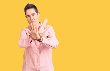 Kısa saçlı, günlük kıyafetler giyen, reddedilen, kollarını kavuşturan, negatif işaretler yapan, kızgın yüzlü genç bir kadın. 