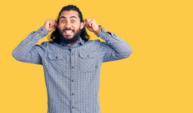 Gündelik giysiler giymiş genç bir Arap gülümseyerek kulaklarını parmaklarıyla çekiyor, komik bir jest. deneme sorunu 