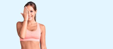 Genç ve güzel İspanyol kadın spor kıyafetleri giyiyor. Bir gözünü eliyle kapatıyor. Yüzünde kendine güvenen bir gülümseme ve sürpriz bir duygu var.. 