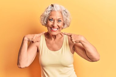 Kıdemli, gri saçlı, günlük kıyafetler giyen neşeli gülümseyen, parmaklarıyla ve ağzıyla işaret eden bir kadın. diş sağlığı kavramı. 