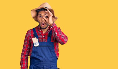 Yakışıklı Latin Amerikalı genç adam tamirci üniforması giyiyor. Şaşırmış yüz ifadesiyle şaşırmış, parmaklarının arasından bakıyor. İnançsız ifade. 