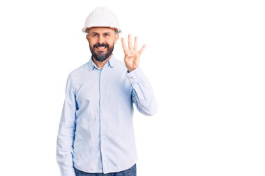 Mimar kasketi takan genç yakışıklı adam kendini beğenmiş ve mutlu bir şekilde gülümserken dört numarayı gösterip işaret ediyor.. 