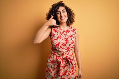 Genç, kıvırcık, güzel bir Arap kadın tatilde. Çiçekli bir elbise ve güneş gözlüğü takıyor. Telefonla el ve parmak hareketleriyle gülümsüyor. İletişim kavramları.