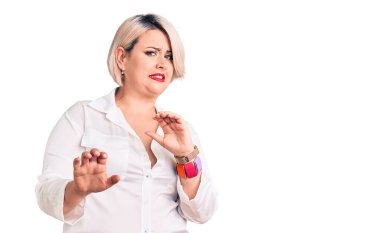 Genç sarışın ve cüsseli bir kadın. Tişört giymiş, tiksindirici bir ifade takınıyor. Tiksinti tepki verdiği için tiksinmiş ve korkmuş bir ifade takınıyor. Eller havada. 