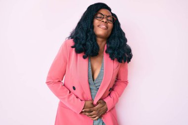 Güzel bir Afrikalı kadın iş ceketi giyiyor ve elleri karnında gözlük takıyor çünkü mide bulantısı, acı verici bir hastalık kendini iyi hissetmiyor. Ağrı kavramı. 