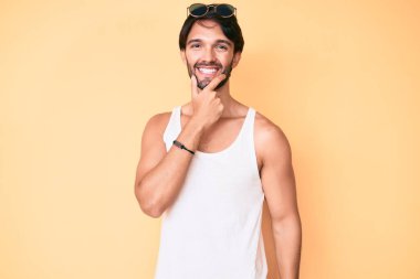 Yaz bakışı ve güneş gözlüğü takan yakışıklı İspanyol adam kameraya kendinden emin bakıyor kollarını kavuşturmuş ve çenesini kaldırmış gülümsüyor. Olumlu düşünmek. 