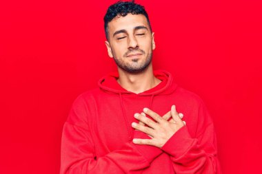 Gündelik kıyafetler giyen genç İspanyol adam elleri göğsünde gülümsüyor, gözleri kapalı ve yüzünde minnet ifadesi var. sağlık kavramı. 