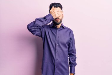 Sakallı, sıradan tişörtlü, eli gözleriyle gözlerini kapatan, ciddi ve üzgün görünen genç yakışıklı bir adam. Görme, saklama ve reddetme konsepti 