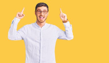 Zarif iş gömleği ve gözlük takan yakışıklı genç adam şaşırmış, şaşırmış ve parmaklarını kaldırıp kollarını kaldırmış.. 