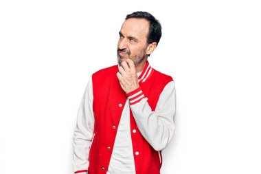 İzole edilmiş beyaz arka plan üzerinde beyzbol ceketi giyen orta yaşlı yakışıklı bir adam çenesinde parmak iziyle şüpheyi düşünüp kafasını kaldırıyor.