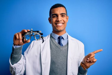 Yakışıklı afro-amerikan optik adam mavi arka planda optometri gözlüğü tutuyor.