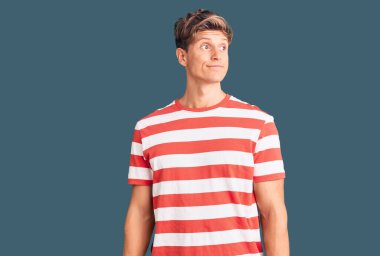 Gündelik kıyafetler giyen genç yakışıklı adam gülümseyerek yan tarafa bakıyor ve düşünüyor.. 