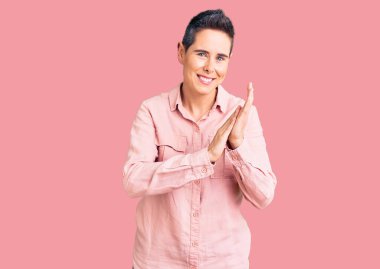 Kısa saçlı, sıradan kıyafetler giyen mutlu ve neşeli alkışlayan, gururlu elleri bir arada tutan genç bir kadın. 