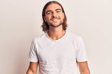 Gündelik kıyafetler giyen yakışıklı genç adam pozitif ve mutlu görünüyor. Duruyor ve gülümsüyor. Kendine güvenen bir gülümsemeyle dişlerini gösteriyor. 