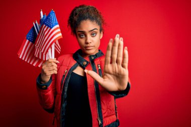 Genç Afro-Amerikan vatansever kız, elinde Birleşik Devletler bayrakları ile izole edilmiş kırmızı arka planda, açık elle dur işareti yapıyor ciddi ve kendinden emin bir ifadeyle, savunma jesti.