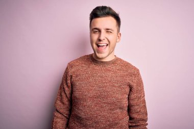 Pembe izole edilmiş arka plan üzerine sıradan bir kazak giyen yakışıklı beyaz adam kameraya seksi bir ifadeyle bakıyor, neşeli ve mutlu bir yüzle..