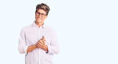 İş kıyafetleri ve gözlük takan genç yakışıklı adam ellerini kavuşturup gülümseyerek gevşemiş ve neşeliydi. Başarı ve iyimserlik 