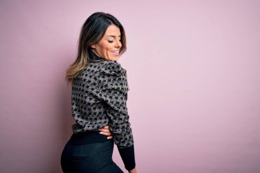 Moda kıyafetleri giyen genç ve güzel bir kadın. Manken, sokak tarzı giyiniyor. Pembe arka planda dikiliyor.