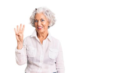 Kıdemli, gri saçlı, günlük kıyafetler giyen, dört numarayı gösteren ve gülümseyen, kendinden emin ve mutlu bir kadın.. 