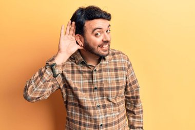 Gündelik kıyafetler giyen, ağzı kulaklarında gülümseyen, dedikoduları ve dedikoduları dinleyen genç İspanyol bir adam. Sağırlık kavramı. 