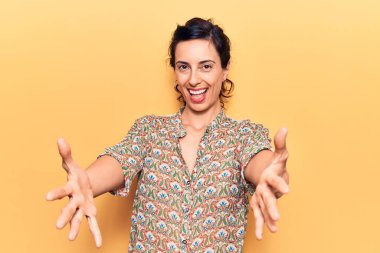 Gündelik giysiler giymiş genç ve güzel bir İspanyol kadın kameraya bakıp sarılmak için kollarını açmış gülümsüyor. Mutluluğu kucaklayan neşeli bir ifade.. 