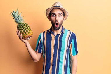 Sakallı, yaz şapkalı, tişörtlü, ananaslı genç ve yakışıklı bir adam. 