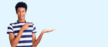 Genç Afro-Amerikalı sıradan kıyafetler giyen adam kameraya hayret ediyor ve gülümsüyor.. 