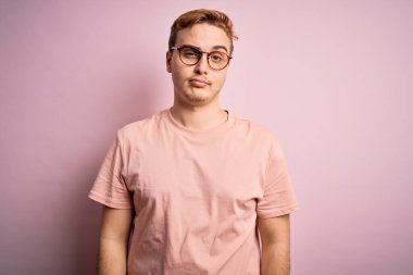 Genç, kızıl saçlı, günlük tişört giyen, pembe arka planda duran, uykulu ve yorgun görünen, yorgunluktan bitkin düşmüş, akşamdan kalma, tembel gözlü bir adam..