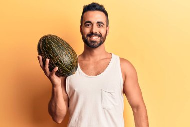 Karpuz tutan genç İspanyol adam pozitif ve mutlu görünüyor. Duruyor ve gülümsüyor. Kendine güvenen bir gülümsemeyle dişlerini gösteriyor. 