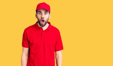 Sakallı genç yakışıklı adam teslimat üniforması giyiyor. Şaşırmış ve şaşırmış bir ifade, korku ve heyecanlı bir yüz ifadesi var.. 